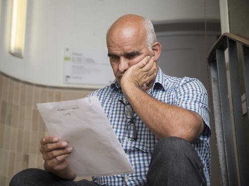 Patient sitz auf einer Treppe im Hausflur und liest besorgt einen Arztbrief, der seinen Krankheitsbefund beschreibt.