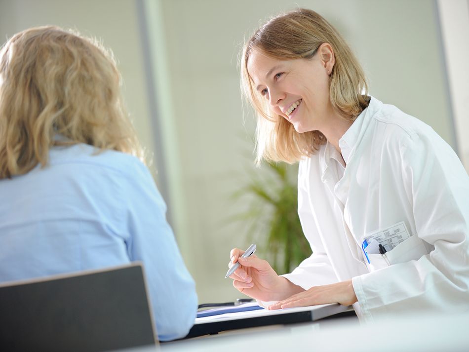 Ärztin am Schreibtisch führt ein freundliches Gespräch mit einer Patientin.