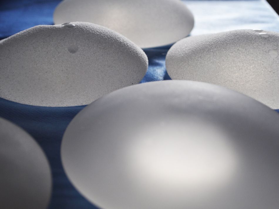 Auf einem Tisch liegen mehrere Brustimplantate aus Silikon, die eine raue Oberfläche haben.